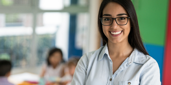 Professora sorrindo em sala de aula conduzindo atividades de alfabetização