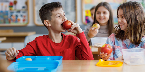 Menino e menina comem maçã e Colégio Talento reforça sobre a alimentação saudável. 